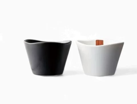Two modern ceramic cups side by side - one black and one white with a wooden handle detail
