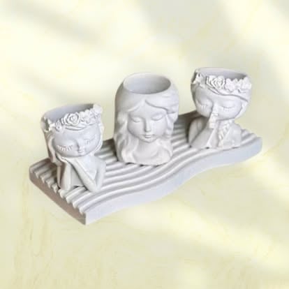 White decorative candle holder with three cylindrical holders featuring ornate rose and face designs on a striped base