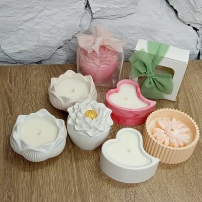Collection of decorative scented candles in various floral designs and colors including white, pink, and peach displayed on a wooden surface