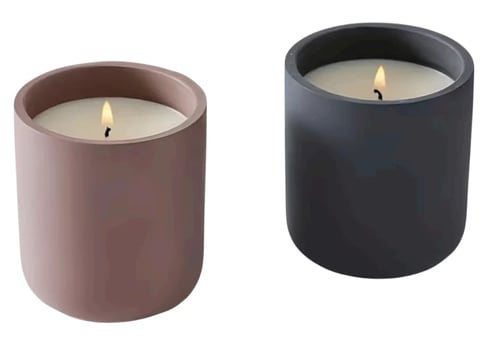 Two cylindrical scented candles in matte finishes - one mauve and one black - each with lit flames inside