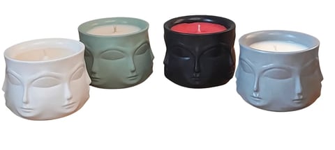 Four decorative face-shaped candles in white, sage green, black, and light blue arranged in a row