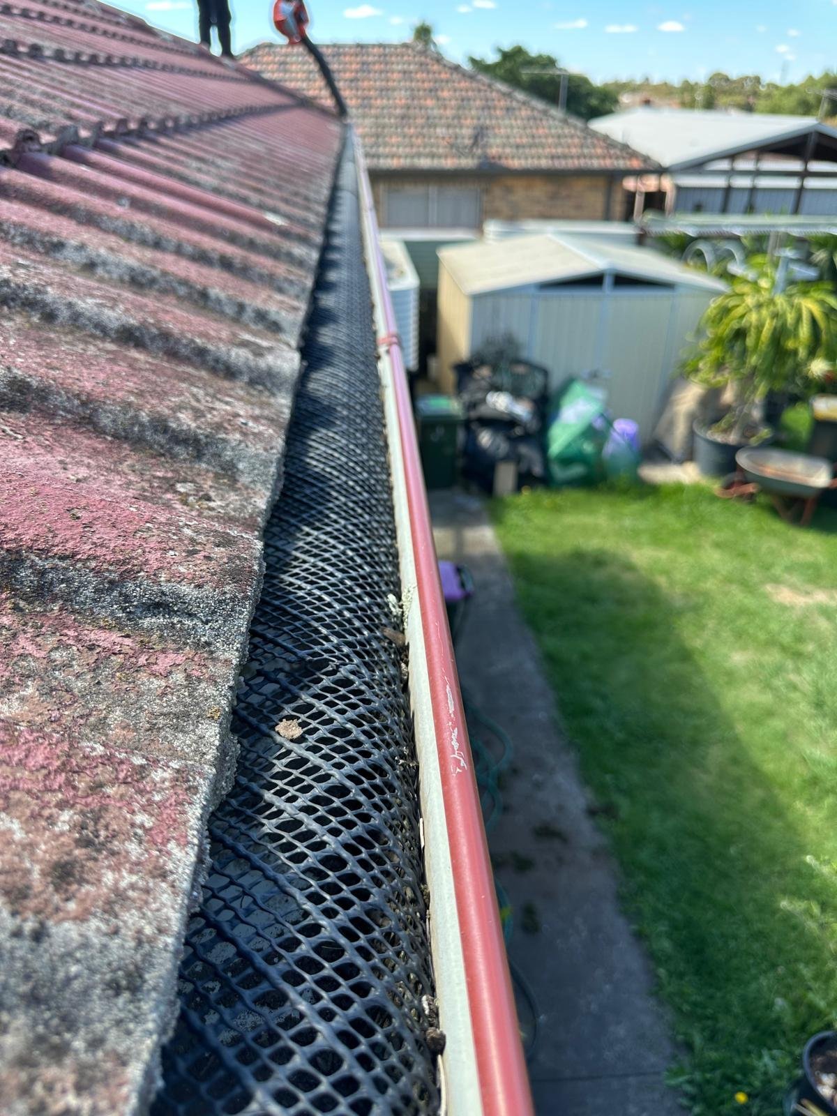 Gutter guard mesh installed on roof gutters overlooking suburban backyard with houses and green lawn