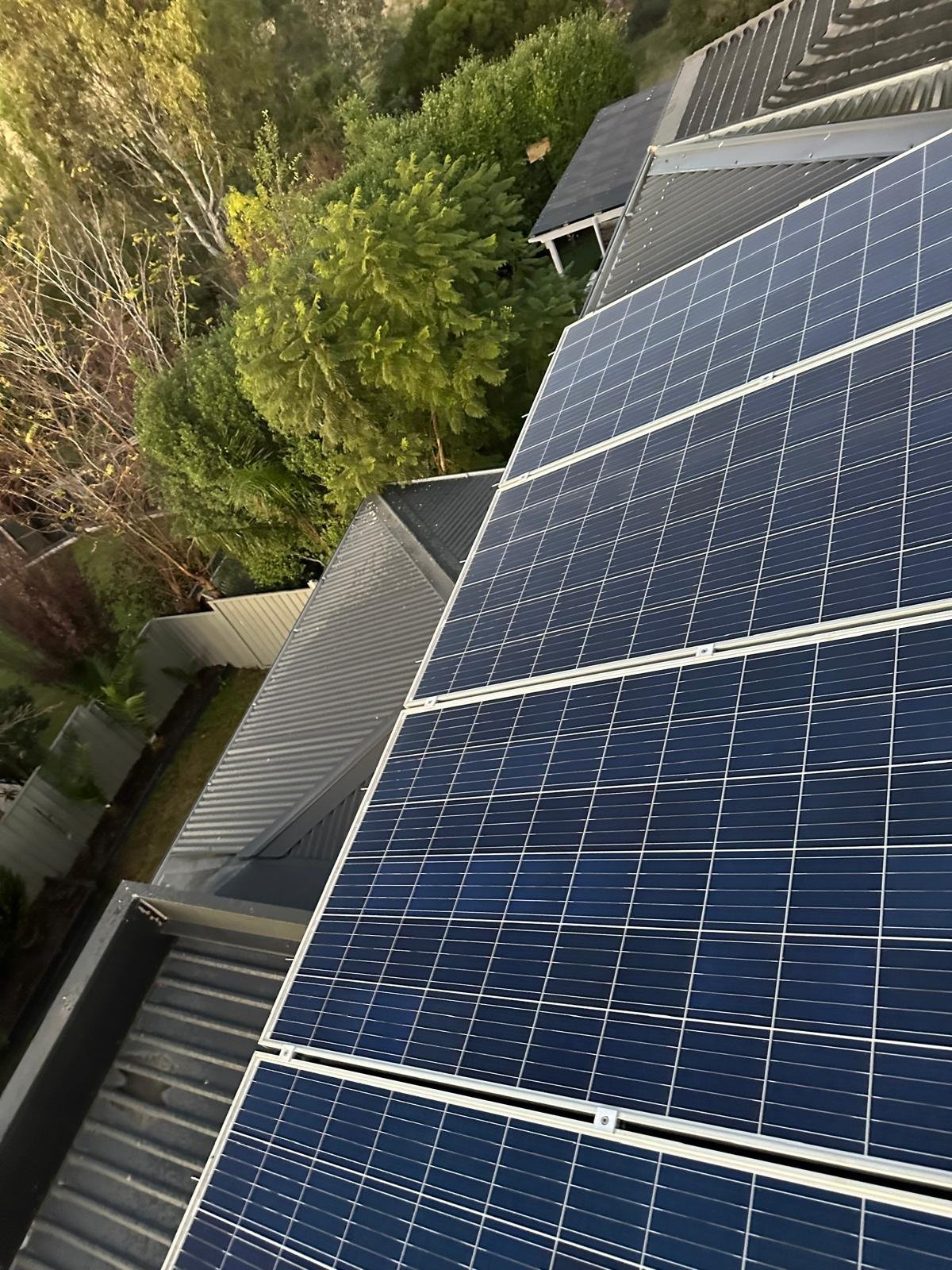Solar panels installed on a residential roof with green trees and surrounding landscape visible
