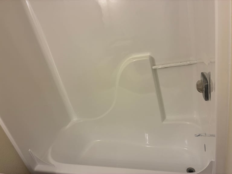 Refinished white bathtub with chrome faucet and shower rod set against beige tile wall