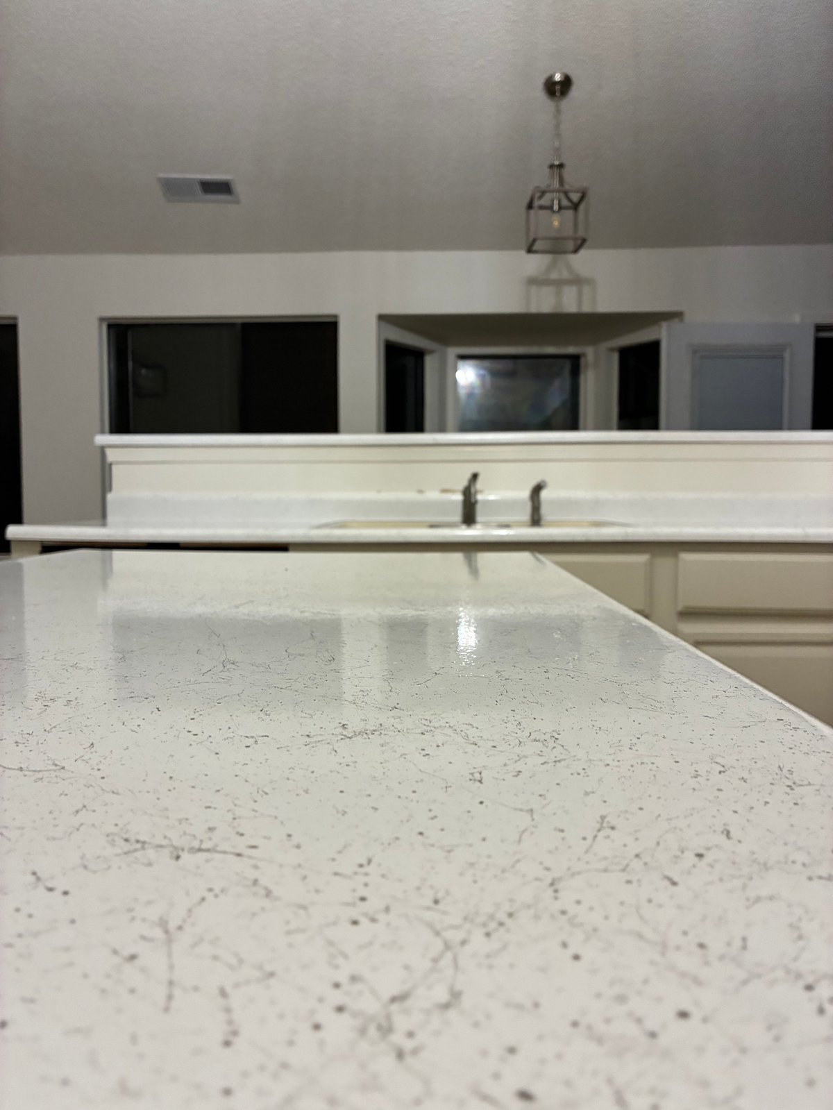 Close-up of light speckled quartz kitchen countertop with white cabinetry and stainless steel fixtures after resurfacing
