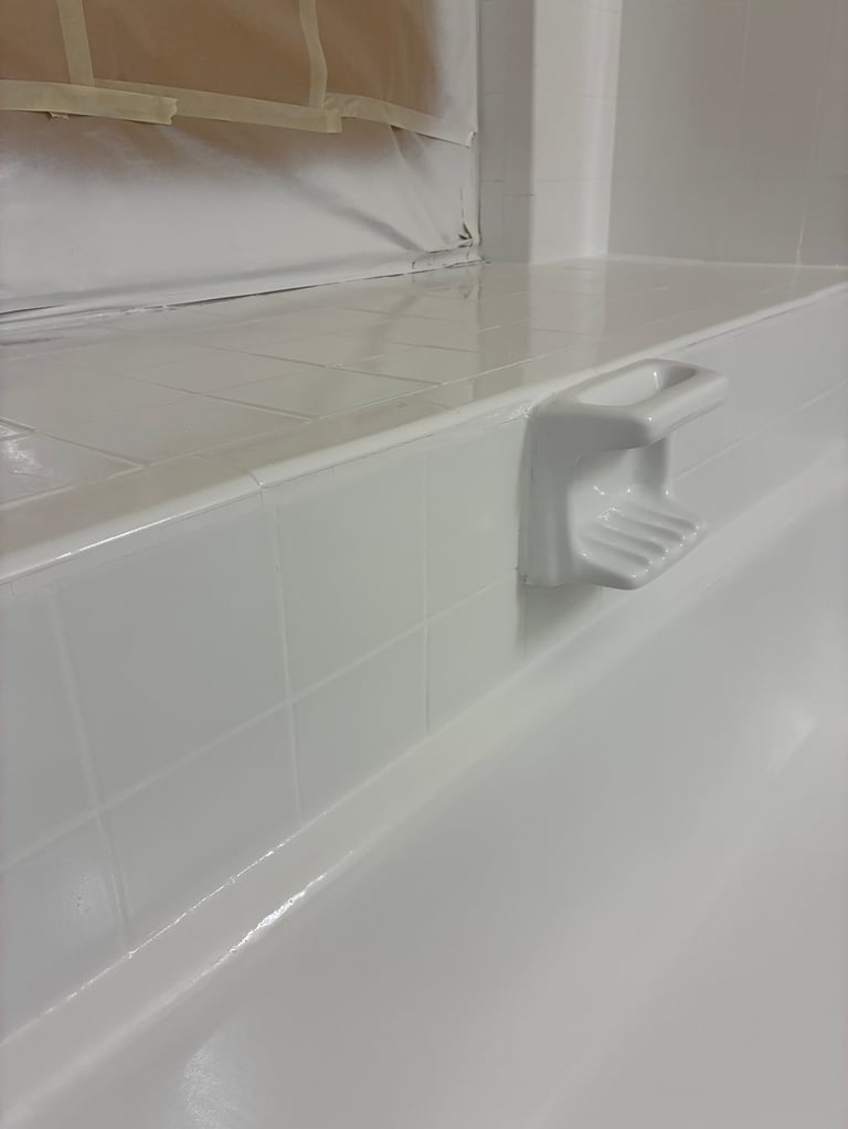 Refinished white bathtub with chrome grip handle and tiled wall with shower enclosure panel