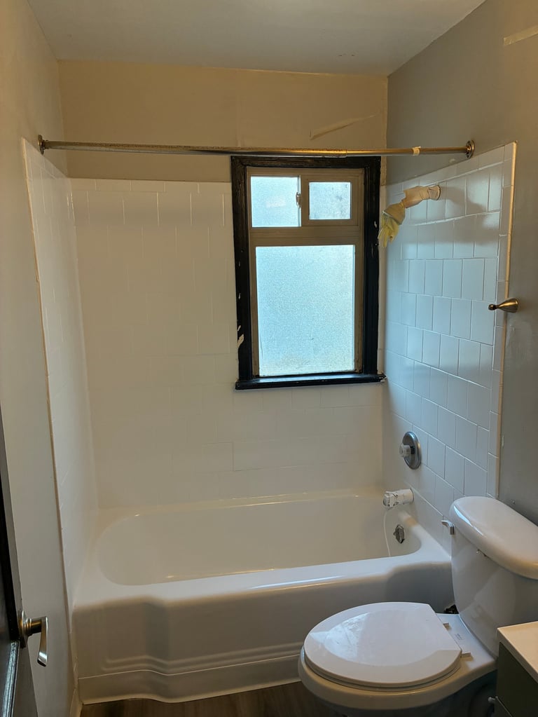 Small bathroom with a resurfaced white bathtub, subway tile surround, and black-framed window