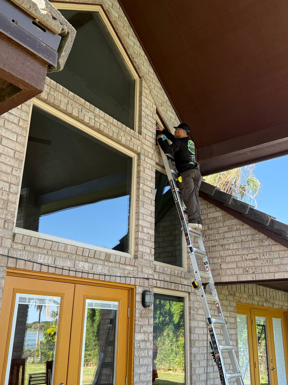 Worker on ladder installing windows on brick building exterior with yellow doors