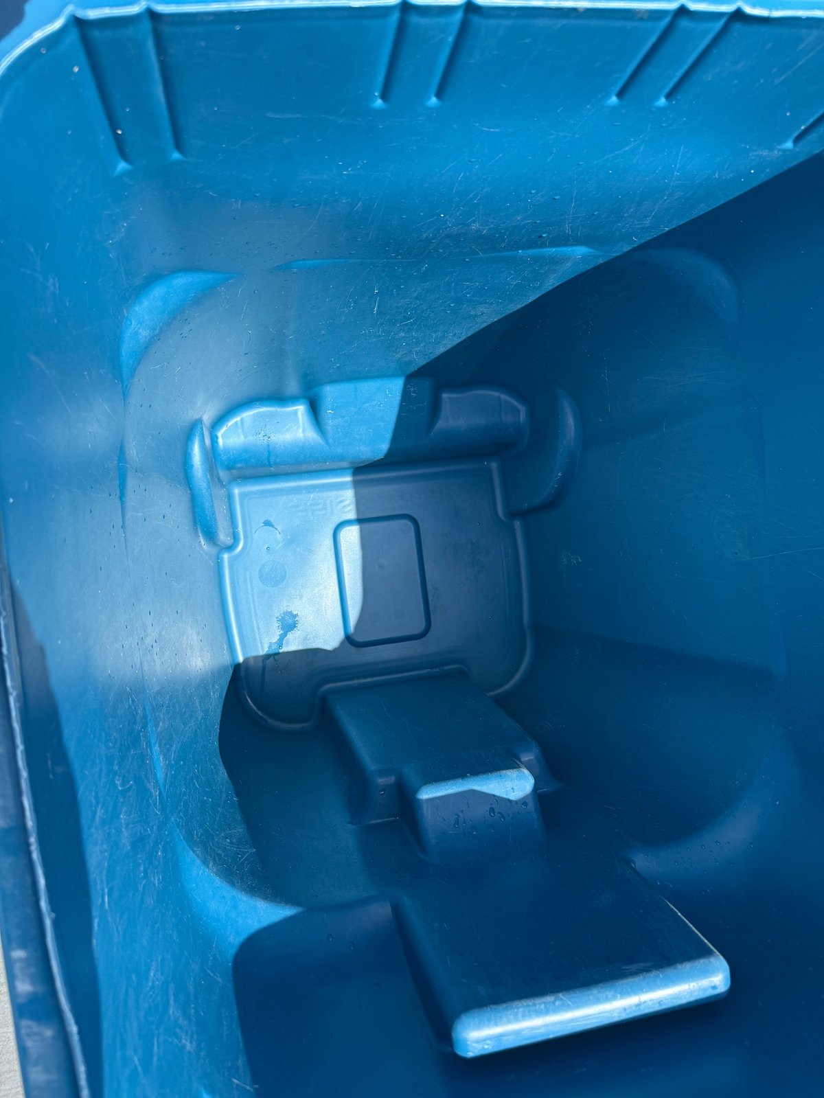 Close-up interior of blue plastic trash or waste bin showing metal latch mechanism and lid hinge details