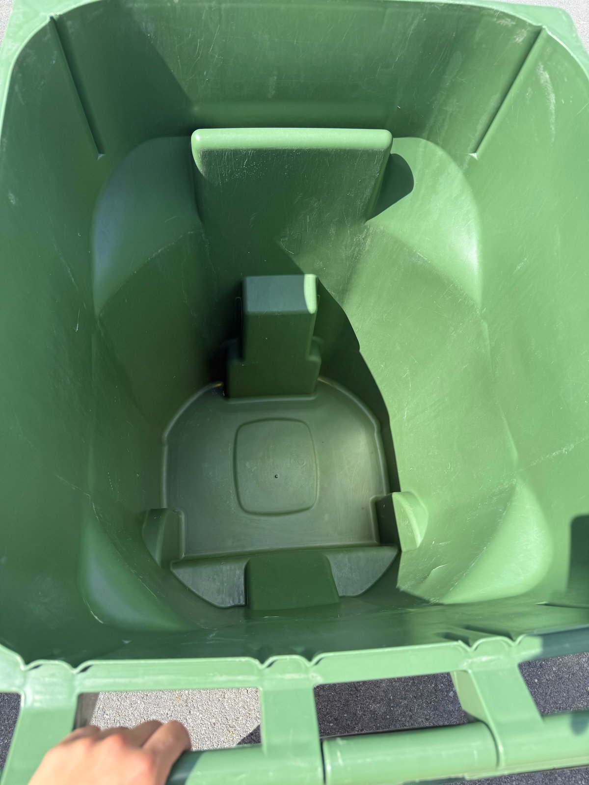 Interior view of a green waste bin showing lid mechanism and bottom compartment with hand reaching in