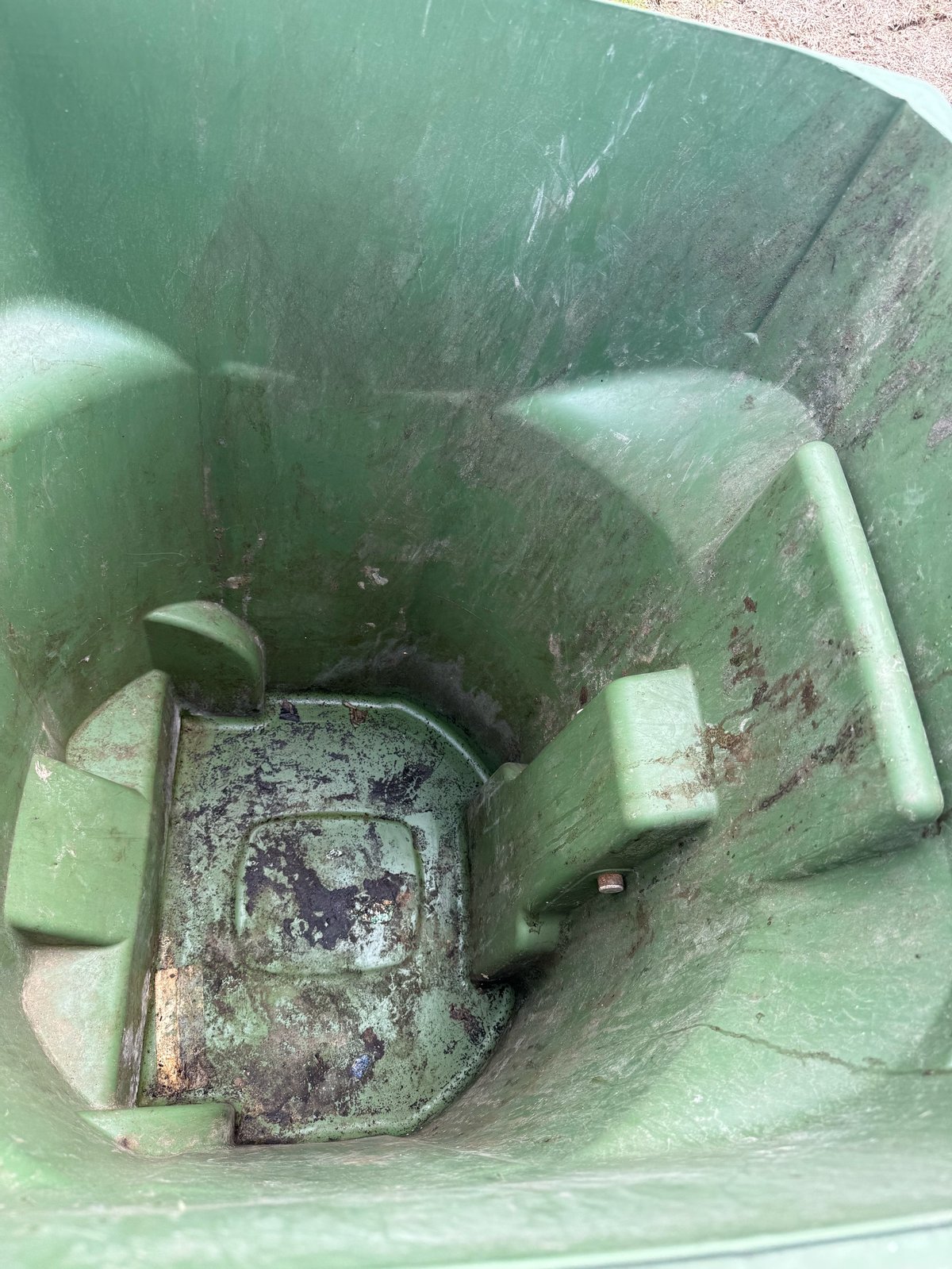 Interior of a green waste bin showing a rusty metal container at the bottom with visible wear and patina