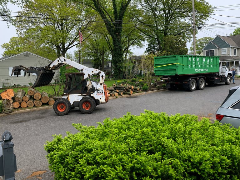 Skid steer loader loading logs onto a green truck — site fully cleared