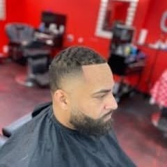 Man with short fade haircut and beard in barber chair, red wall background