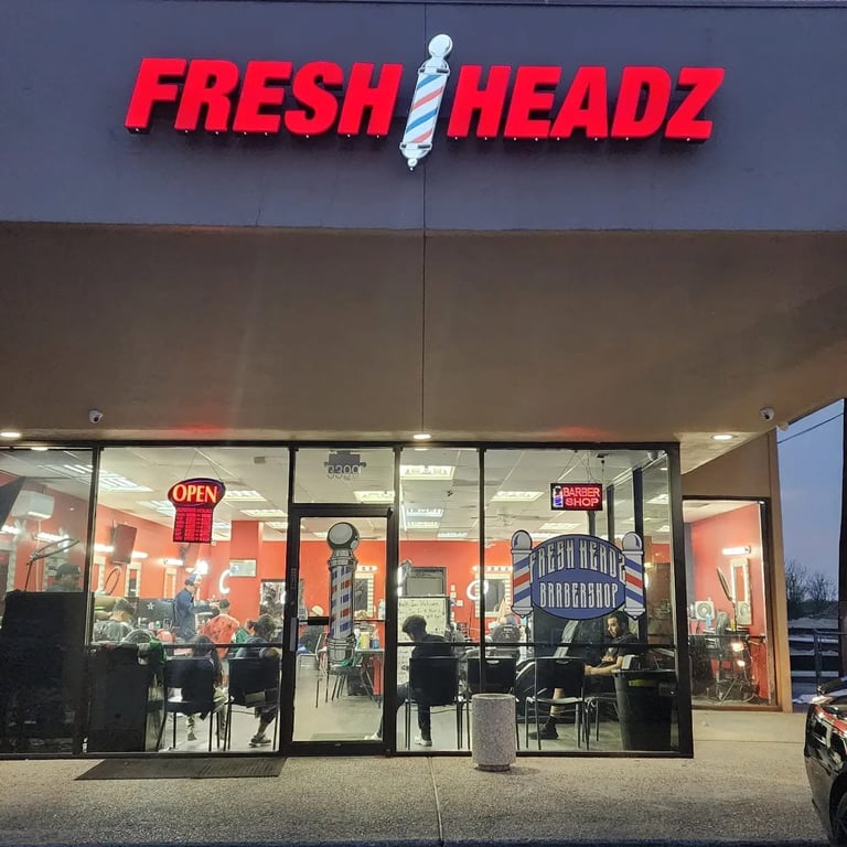 Fresh Headz barbershop storefront with red neon sign, large glass windows, and interior seating visible at dusk