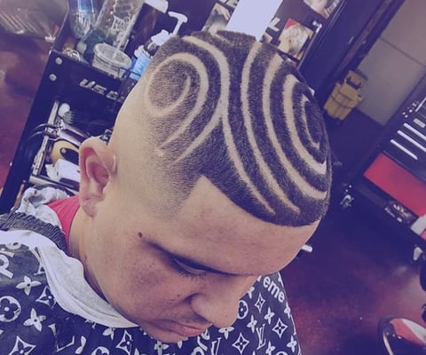 Person with a bold geometric spiral and wave design shaved into their blonde hair, displayed from a side profile view
