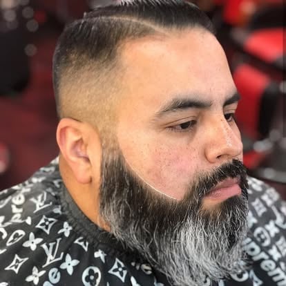 Man with long dark beard and short hair wearing patterned black shirt, photographed in profile