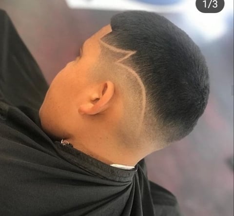 Side view of a person with a modern haircut featuring short faded sides and geometric line designs shaved into the undercut