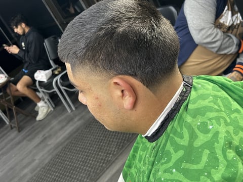 Back of a persons head wearing a green patterned shirt, surrounded by other people in an indoor setting