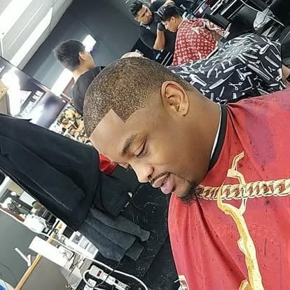 Man in red and black jacket with gold trim looking down in a barber shop setting