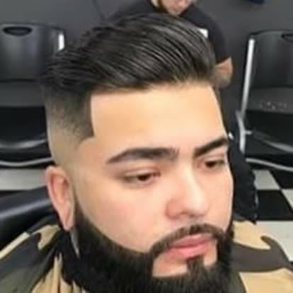Man with dark undercut hairstyle, full beard, wearing black and tan striped shirt in barbershop setting
