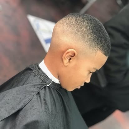 Side profile of a young boy with a short, faded haircut wearing a black collared shirt
