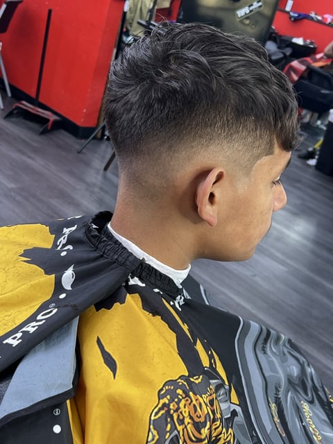 Side profile of a mans short fade haircut with textured top, wearing a yellow and black jacket in a barber shop