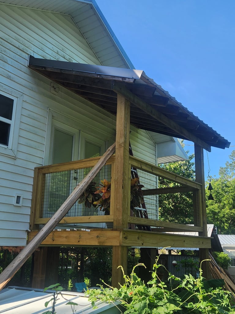 Wooden porch with pergola on light green house, featuring mesh railings and wooden support beams, clear sky