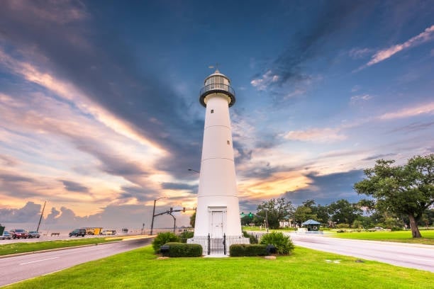 White lighthouse standing in green landscape at sunset with dramatic cloudy sky