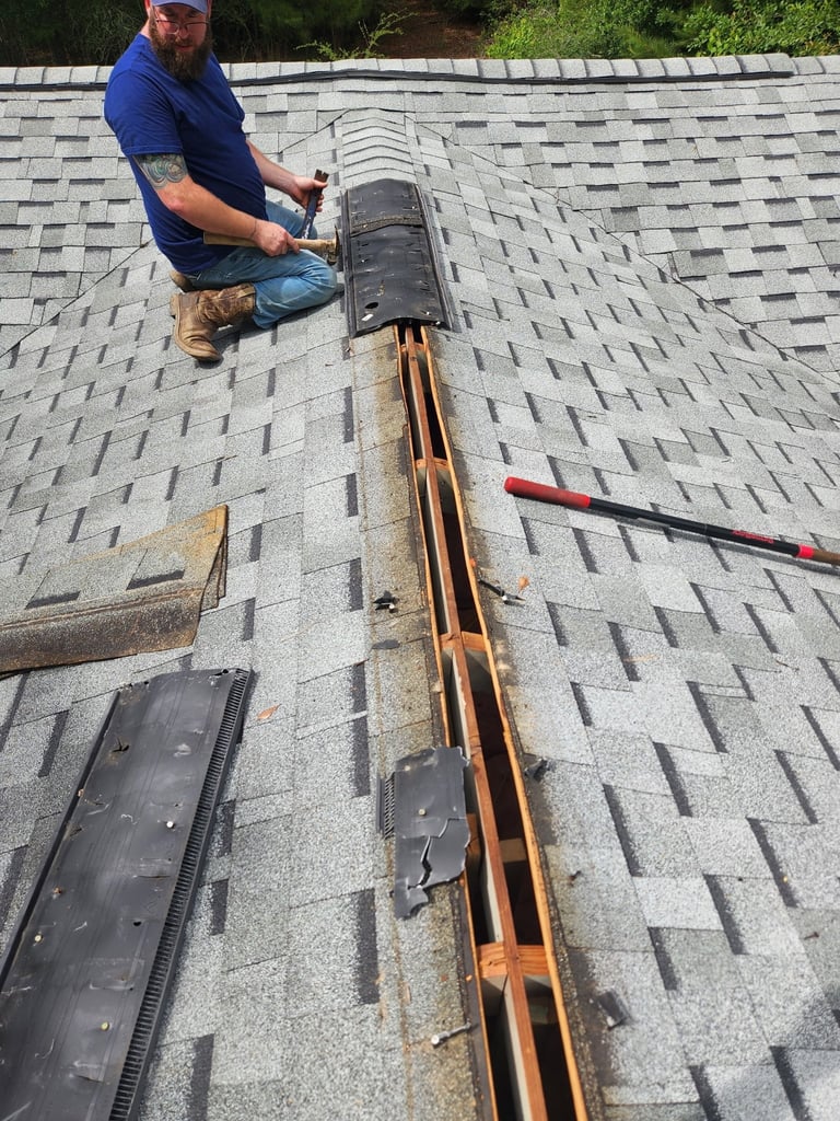 Roofer in blue shirt installing gutter system on gray asphalt shingle roof with tools nearby