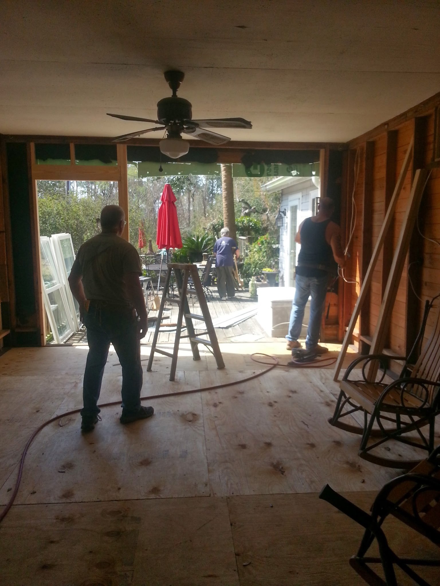 Interior view of a sunroom with people standing on a concrete floor, looking out through open glass doors toward a patio