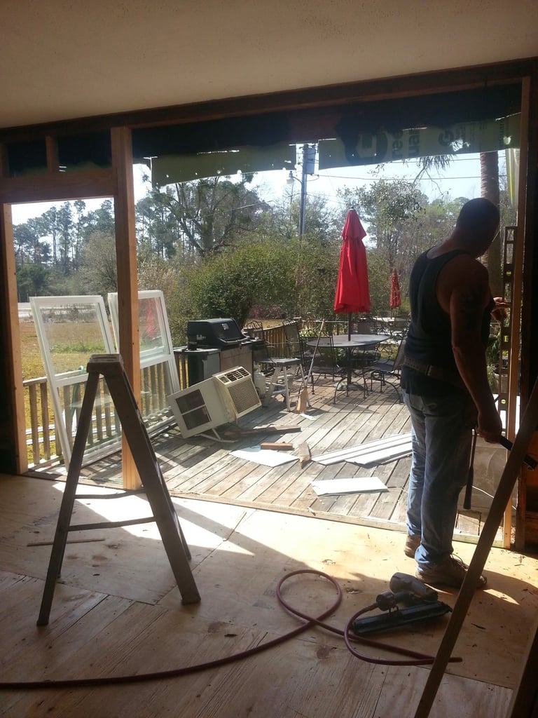 Person standing in doorway looking out onto wooden deck patio with red umbrellas and outdoor furniture