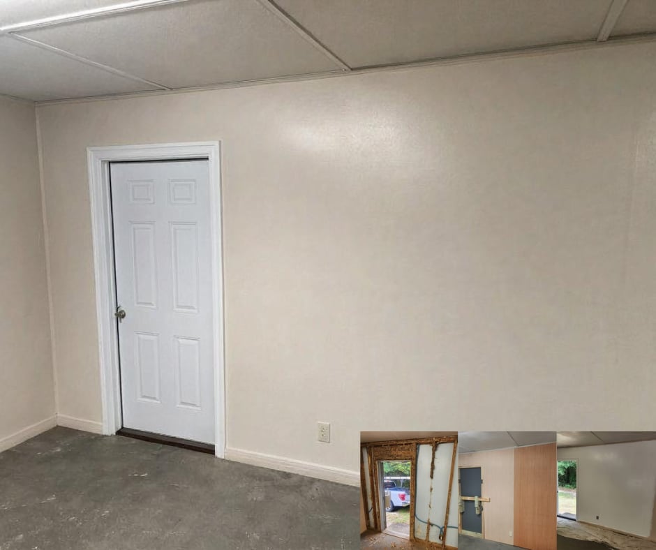 Empty basement room with white six-panel door, beige walls, drop ceiling, concrete floor, and cardboard boxes stacked in corner