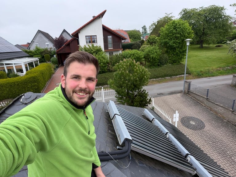 Man in bright green hoodie taking selfie on roof with solar panels and suburban houses in background