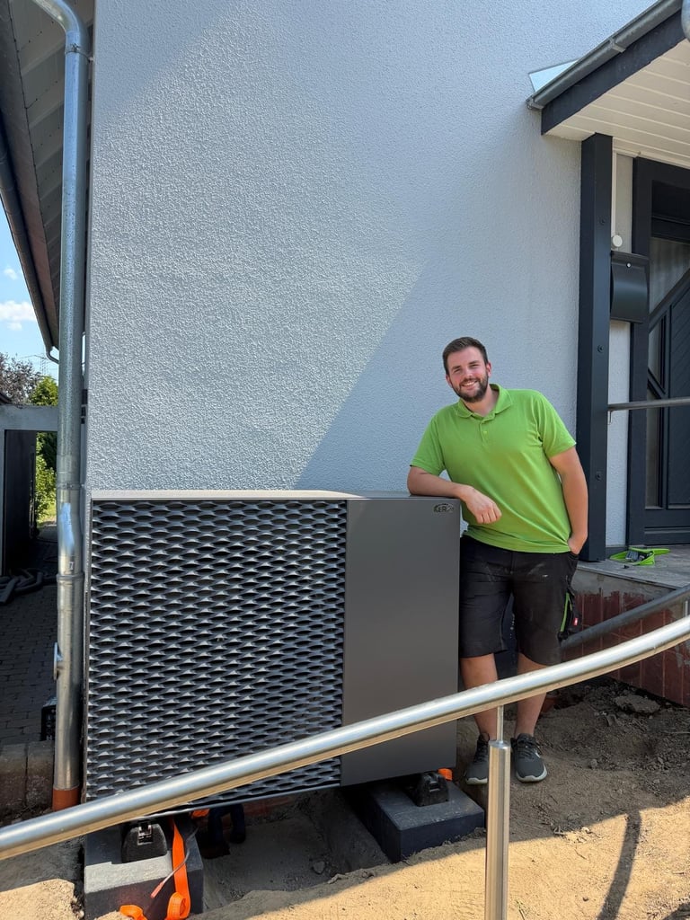 Man in green shirt standing next to an HVAC unit outside a white house