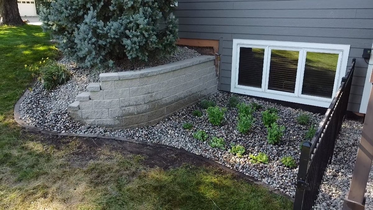 Modern home foundation with curved stone retaining wall, gravel landscaping, and triple sliding glass doors with black trim