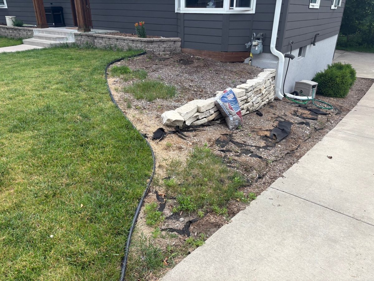 Backyard landscaping project with mulch beds, edging, and pavers during installation next to house