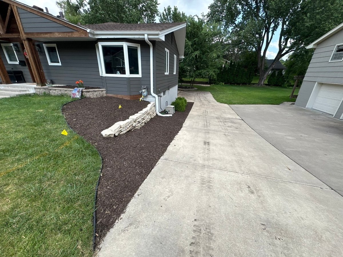Modern home with gray siding, driveway, mulched landscaping bed with white rock border, and manicured lawn in suburban neighborhood