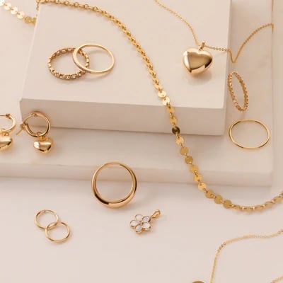 Collection of gold jewelry including rings, necklaces, and bracelets displayed on a white platform and surface