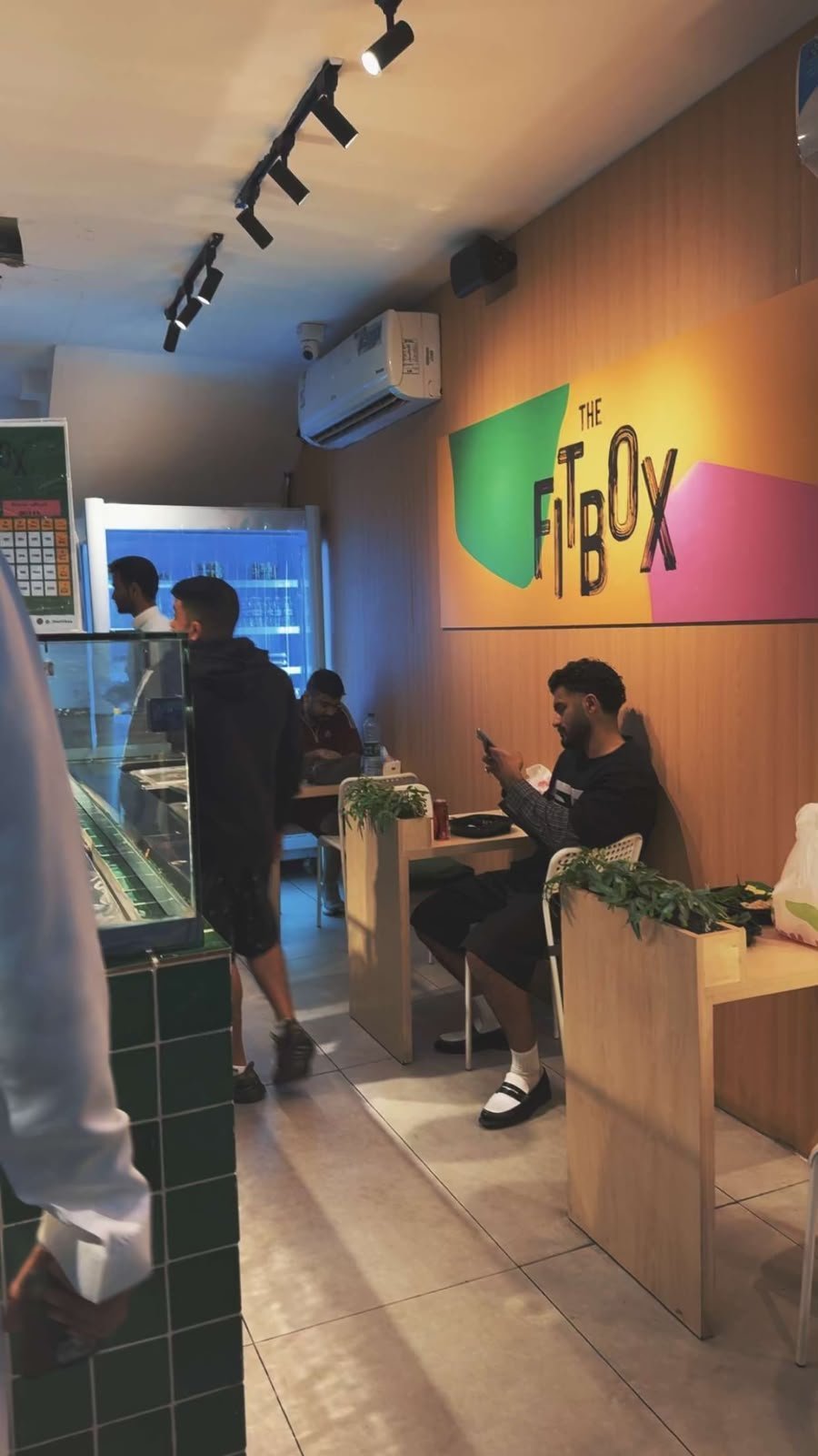 Interior of The Box restaurant with customers at counter and seating area, colorful signage, track lighting, and modern decor
