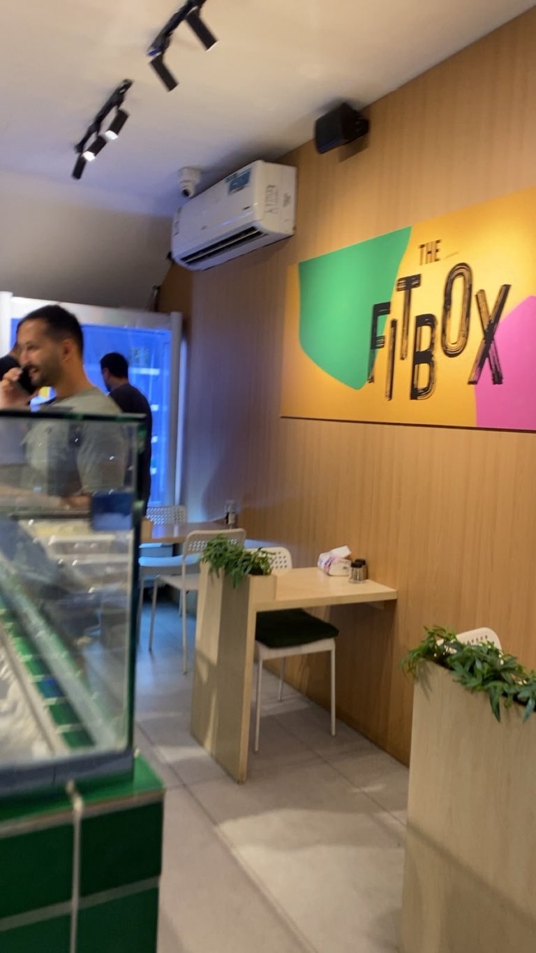 Interior of The Fitbox restaurant with colorful logo sign, wooden walls, counter service area, and modern lighting fixtures