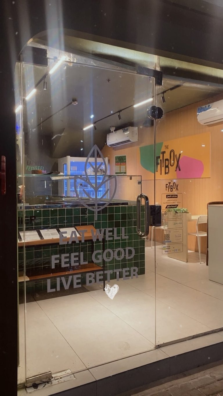 FitBox gym storefront with glass doors displaying motivational text Feel Well, Live Better and neon signage at night