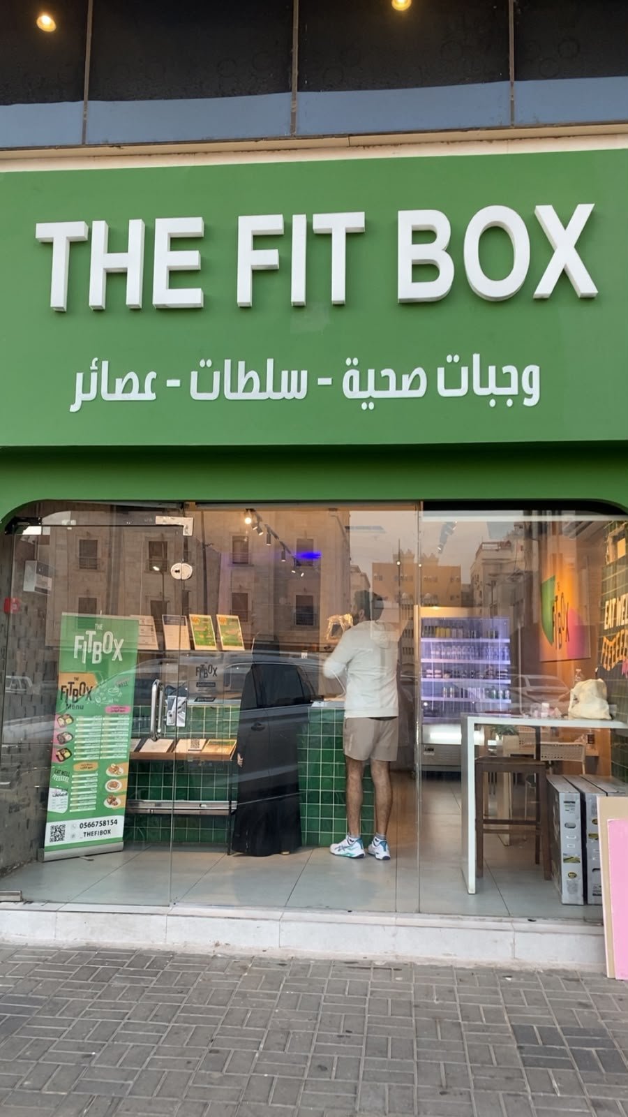 The Fit Box storefront with green signage and Arabic text, displaying fitness products and clothing in the window display