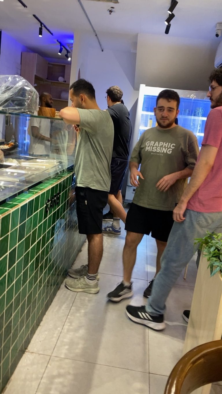 Group of people waiting in line at a modern cafe counter with blue lighting and tile accents
