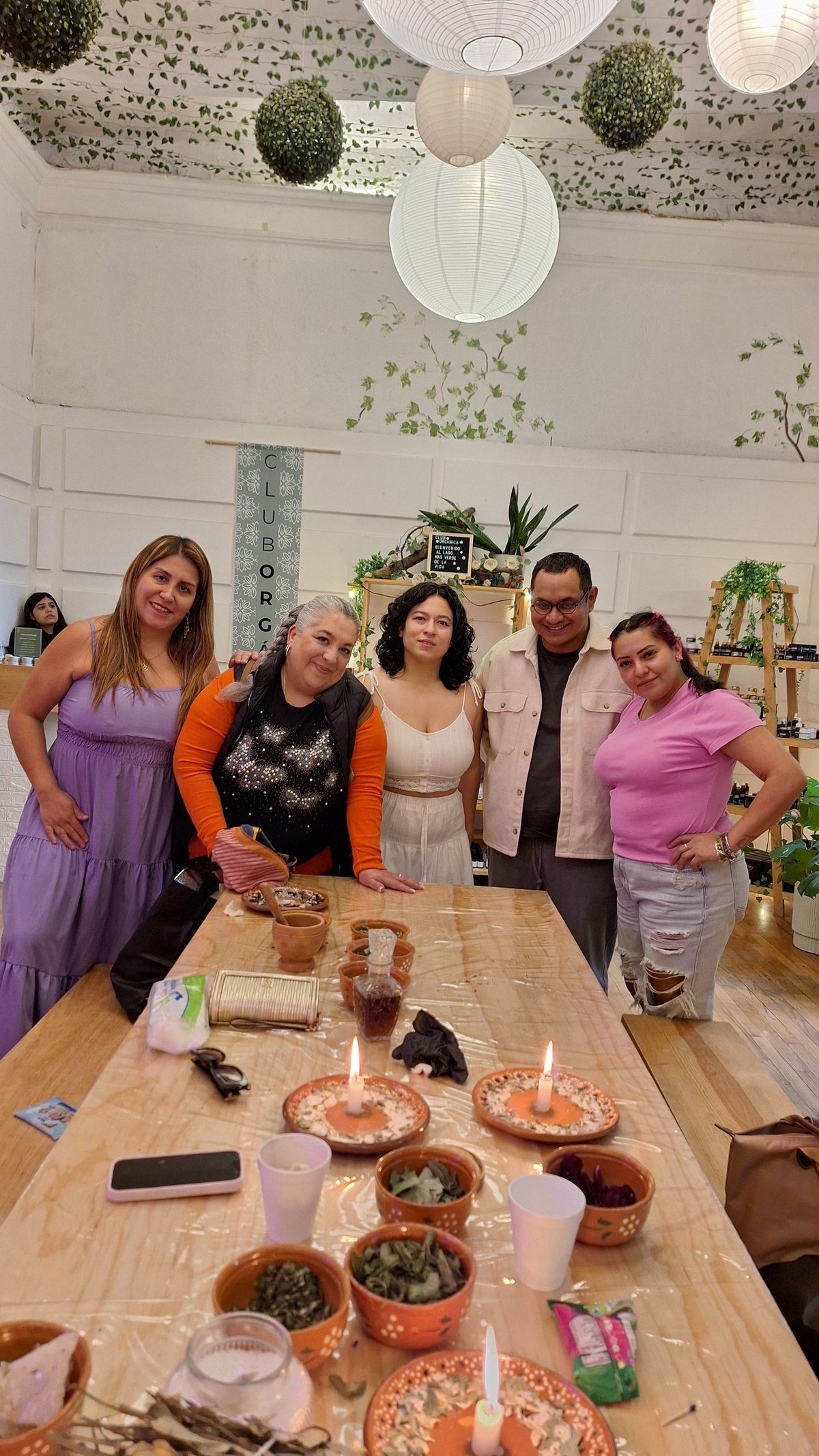 Cinco personas de pie detrás de una mesa con velas encendidas, hierbas, cuarzos y materiales de práctica durante una experiencia presencial de Mágica Expresión