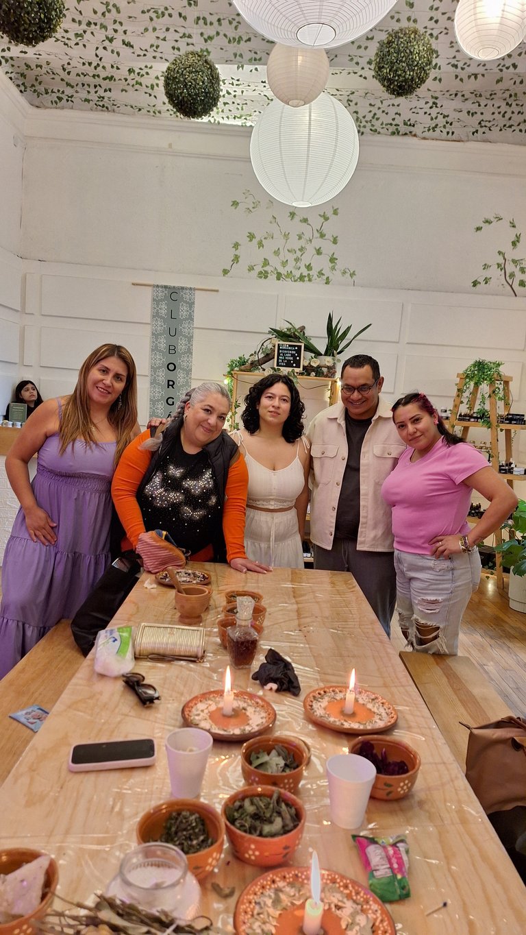 Cinco personas de pie detrás de una mesa con velas, alimentos y plantas durante una celebración en un salón con decoración botánica