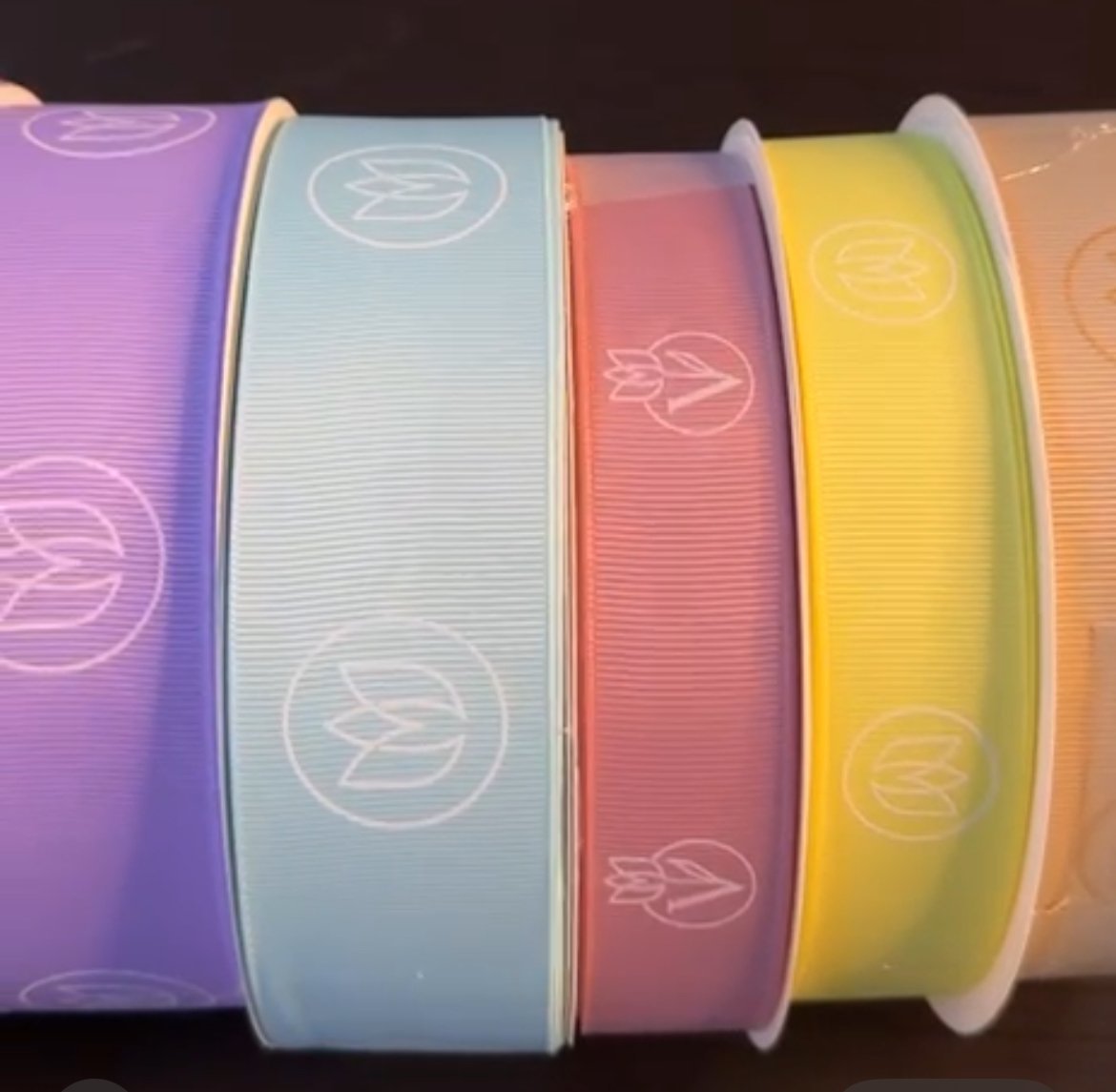 Five colorful ribbon rolls with peace symbol patterns in purple, blue, coral, yellow, and peach arranged in a row