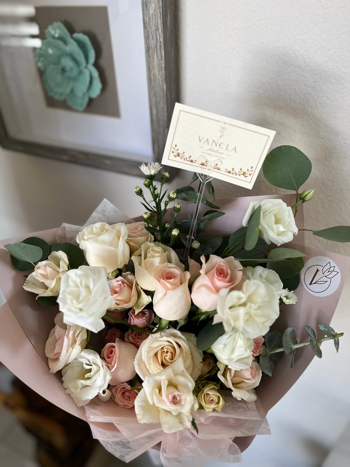 Elegant bouquet of white and pink roses wrapped in dusty pink tissue with personalized name card and decorative elements