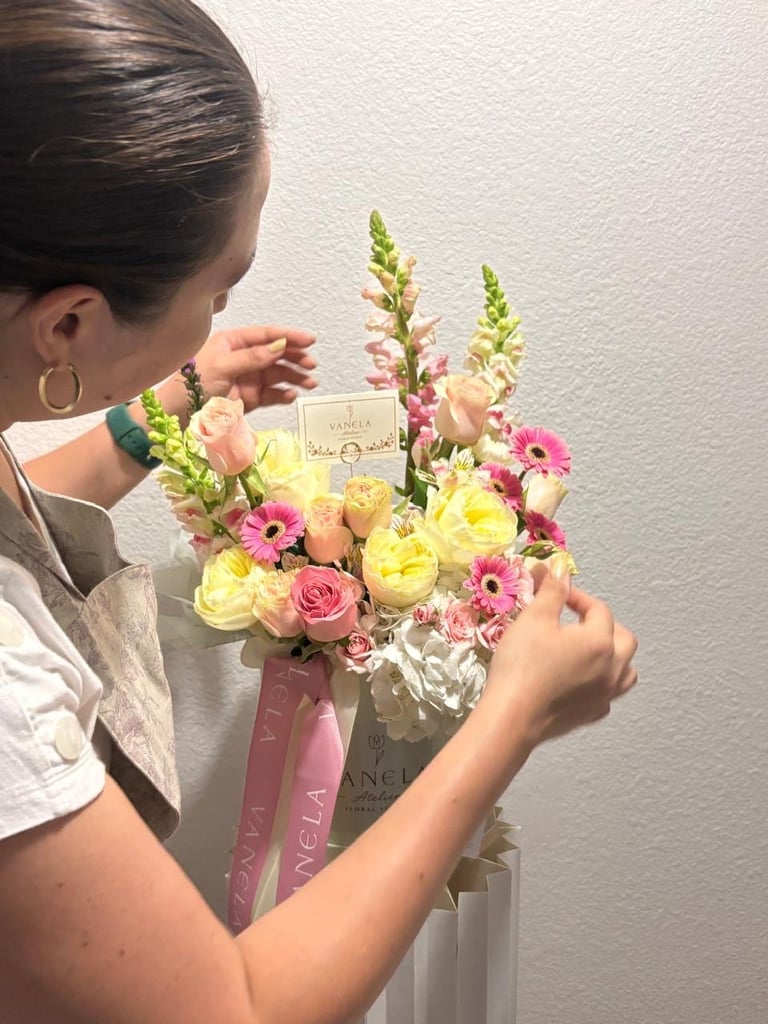 Woman holding a colorful floral bouquet with pink roses, yellow flowers, and green stems, with shopping bags attached