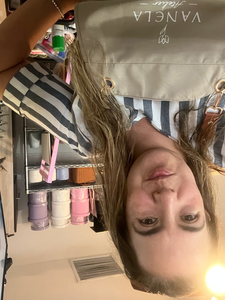 Person holding a cosmetic product in front of a striped bag in a bathroom, photographed upside down