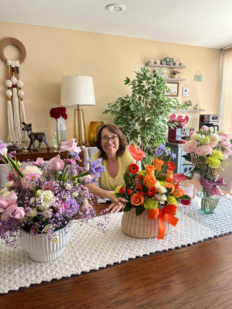 Woman surrounded by colorful flower arrangements in vases on a white textured table in a bright living room
